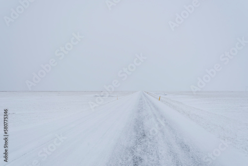 Straight icy road on a remote location in Iceland during winter with almost no difference between the snowy land and sky.