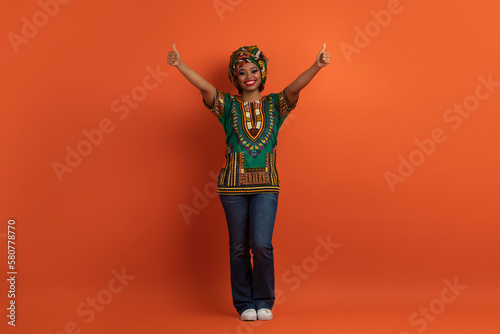 Cool cheerful african woman in national costume showing thumb ups © Prostock-studio