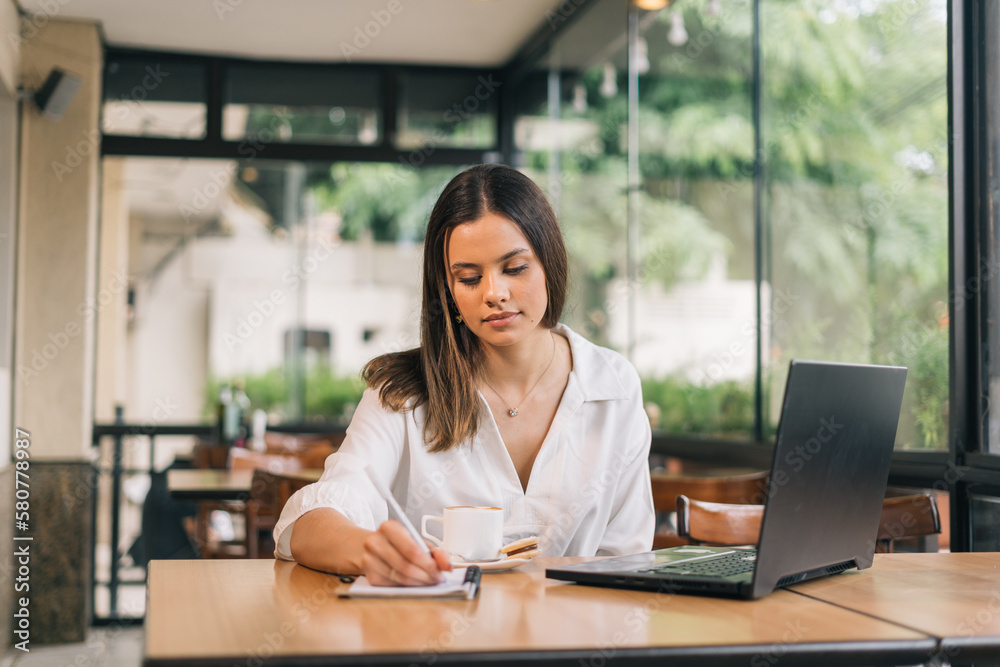 In charge of monitoring social networks, watching online video reflecting on how to create publication by writing in notebook. Female administrative assistant checking information and data
