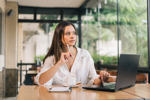 Development of a new business strategy. View of a young business woman in formal clothes thinking about something and looking at the laptop while sitting in the modern office