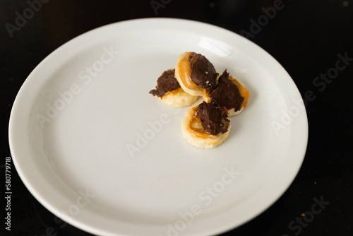 four pieces of frozen banana with peanut butter and melted chocolate with flaky salt on white plate  copy space