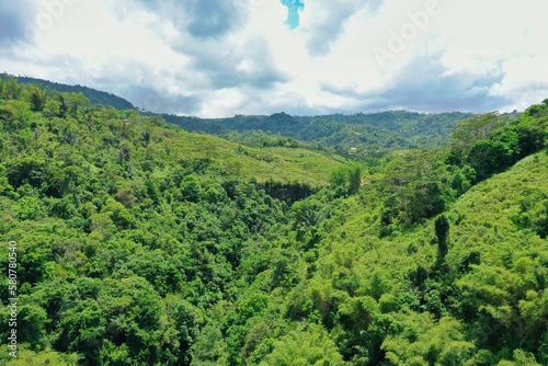 Panorama drone shot from above of a rainforest valley on Flores, in the distance a rice terrace, hills and a blue cloudy sky. photo