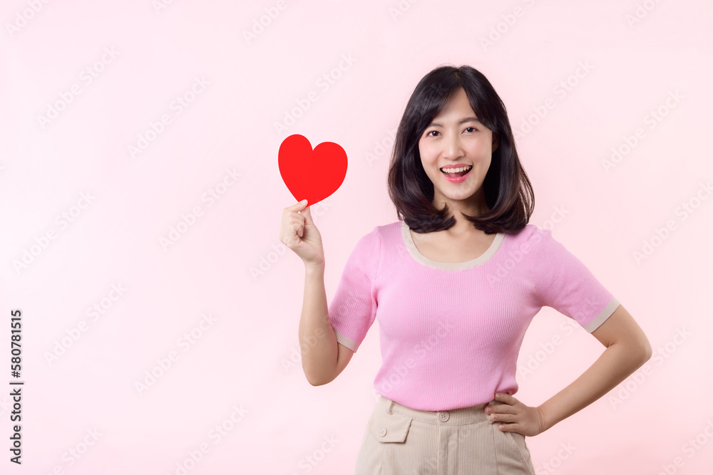 Young asian woman happy tender smile holding paper card love sign isolated on pastel pink background. Romantic valentine holiday, wellness, insurance, healthcare, wellbeing concept. Young asian woman happy tender smile holding paper card love sign isolated on pastel pink background. Romantic valentine holiday, wellness, insurance, healthcare, wellbeing concept.