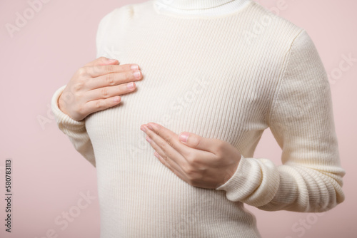 Woman hands checking lumps on her breast for signs of breast cancer on pink background. Healthcare world health day concept.