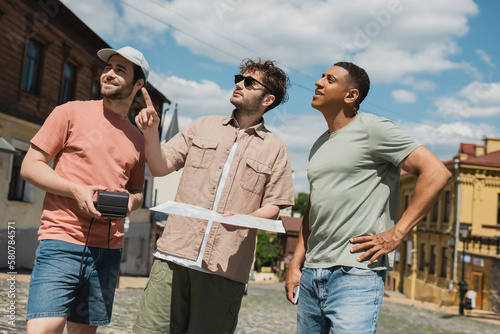 guide in sunglasses holding city map and pointing with finger while leading tour for multiethnic travelers on Andrews descent in Kyiv.