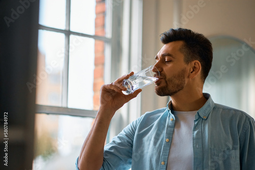 Thirsty man having glass of water at home.