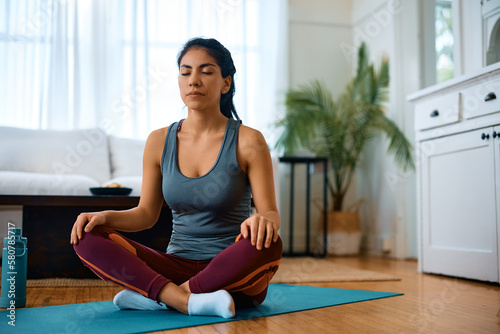 Athletic woman meditates with eyes closed while practicing Yoga at home.