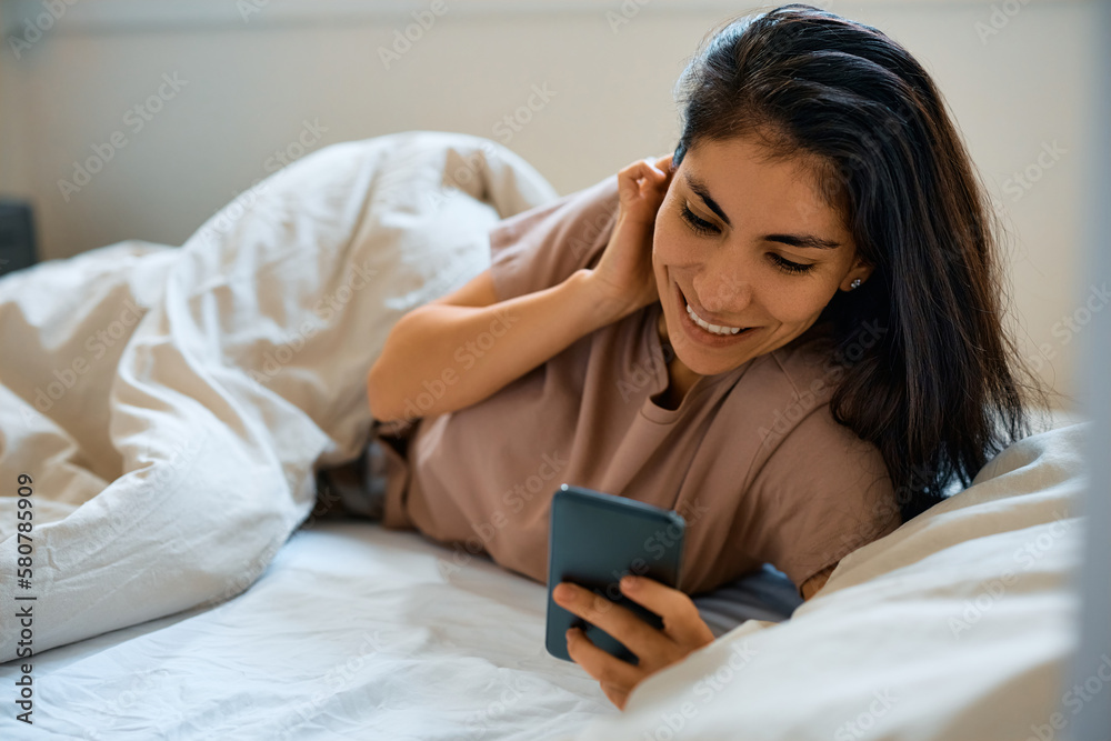 Happy woman using smart phone while relaxing in bed. Happy woman using smart phone while relaxing in bed.