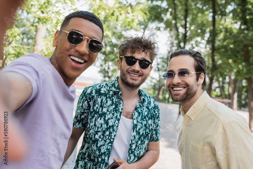 Positive multiethnic friends in sunglasses spending time in park in summer.