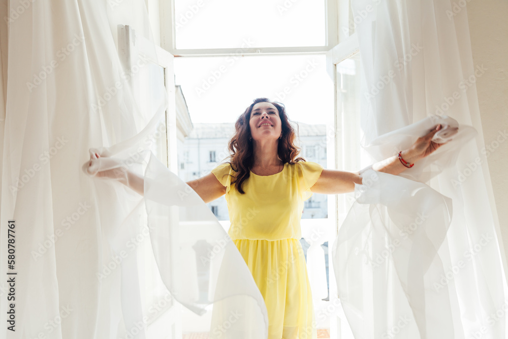 beautiful brunette woman in a yellow dress stands in a bright room by the window beautiful brunette woman in a yellow dress stands in a bright room by the window