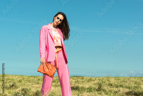 Spring outfits. women's bag of a stylish girl in a jacket suit and pink pants posing for the camera. Urban style women's handbag. Vivid orange women's bag