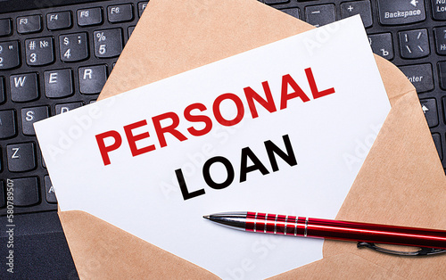 White card with the text PERSONAL LOAN in a craft envelope on a work desk with a modern laptop keyboard and burgundy pen. Flat layout of the workplace. photo