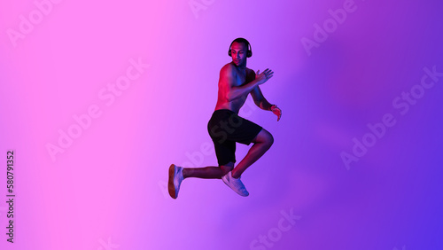 Athletic African American Male Jumping Wearing Headphones Over Purple Background
