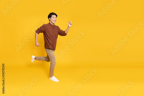 Side view of full length portrait of Asian young businessman walking isolated on yellow background