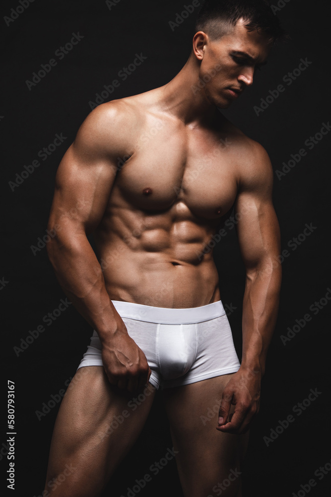 Handsome young man in a white underwear posing over black background. Perfect body and skin. Studio shot.