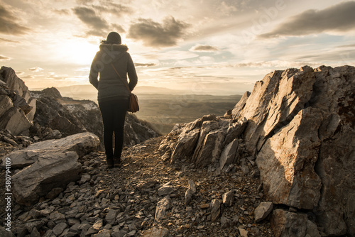 A woman stands with her back on the edge of the cliff. Rocky mountain at sunset.