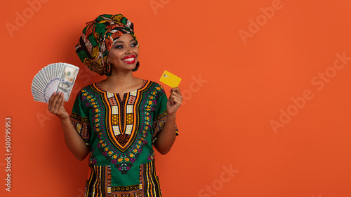 Happy black woman in african costume holding cash, bank card