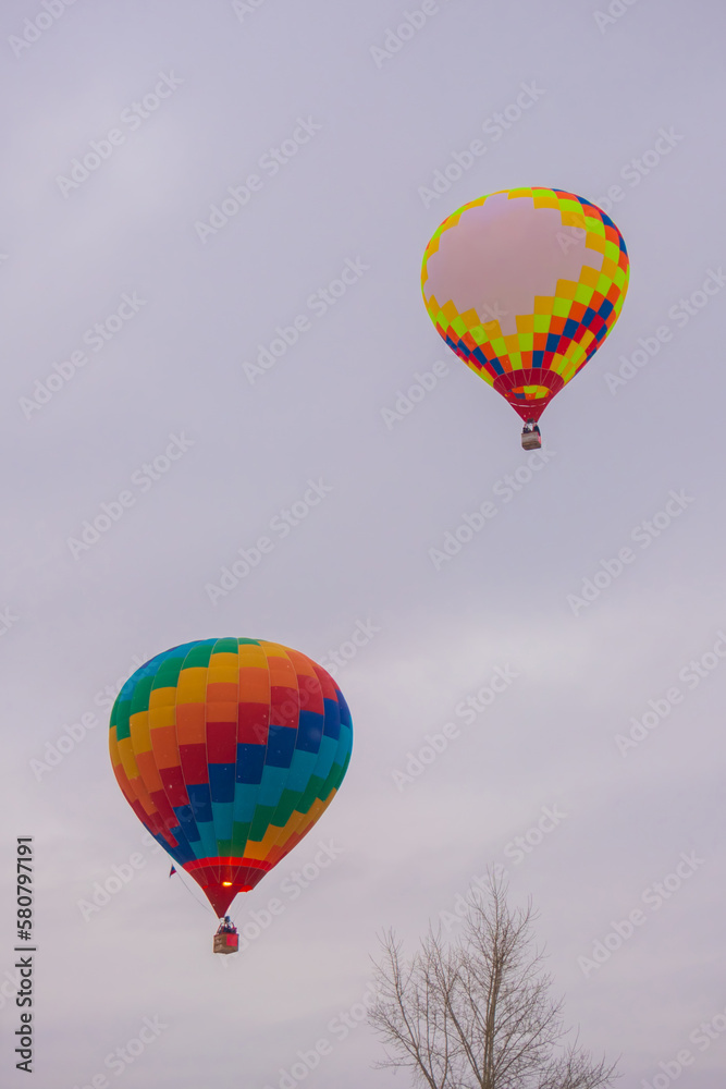 Naklejka premium Two colorful hot air balloons flying against grey sky at Winter aerostat festival. Freedom, sport, aircraft concept
