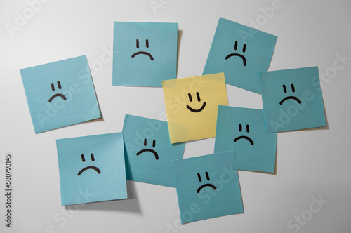 Sticker notes on the white background. Sticky note papers with smiley. One is different. One happy smiling face among sad ones. 