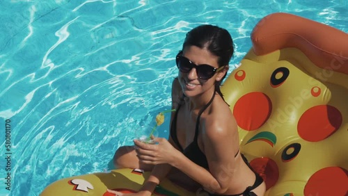 Beautiful young female in swimming pool enjoying summer and drinking cocktail. Sexy woman in bikini enjoying summer sun and tanning during holidays in pool with cocktail. Slow motion