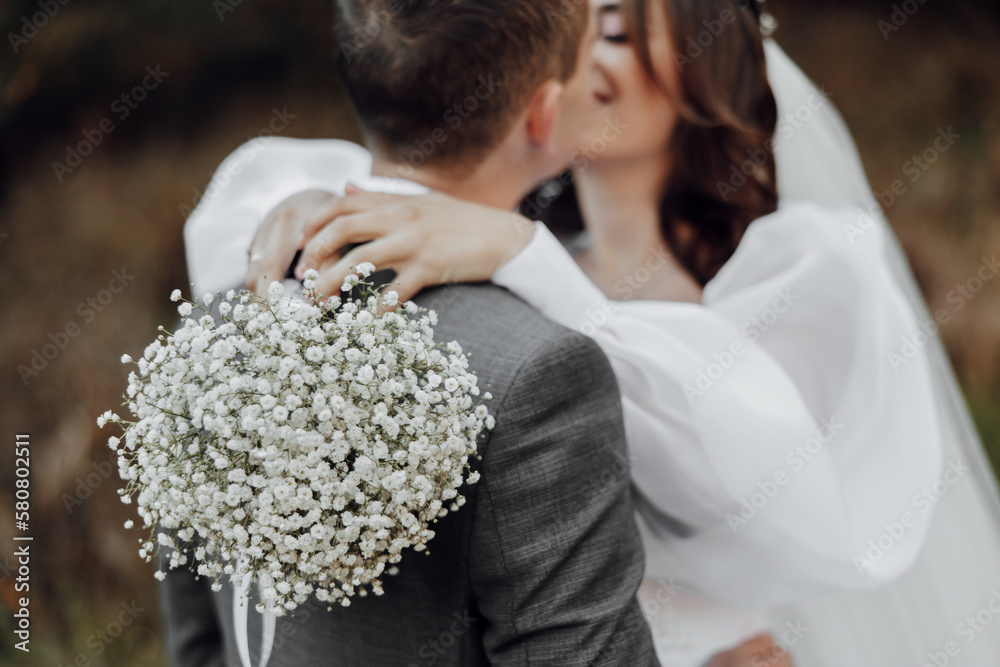 the bride holds a wedding bouquet of white flowers in her hands. Hugs the groom. Tenderly kisses the bride. the bride holds a wedding bouquet of white flowers in her hands. Hugs the groom. Tenderly kisses the bride.