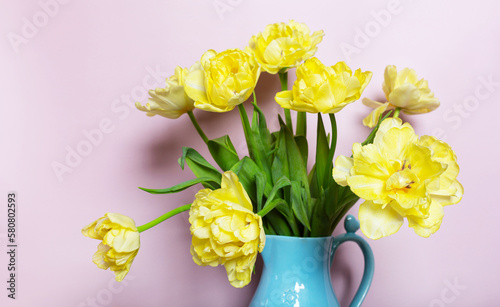 Bouquet fresh yellow tulips in blue ceramic jug on pink background. Bright spring bouquet for home decor. Concept: birthday, women's day, greeting card..