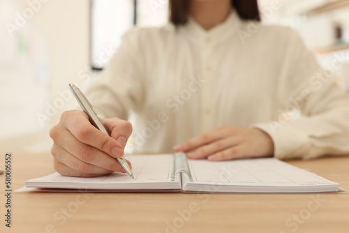 Business woman takes notes in organizer at table in office.