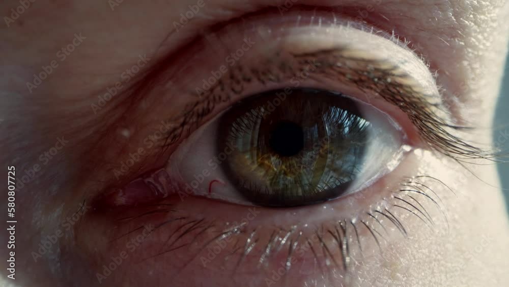 Macro of an opening eye with a beautiful green iris, a tired look with a burst vessel of an aged woman