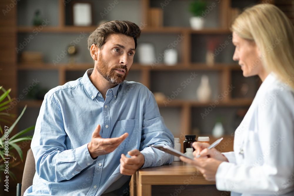Fototapeta premium Male Patient Sharing Health Problems With Doctor Woman During Meeting In Office