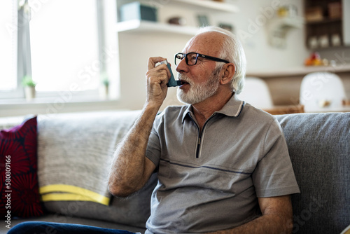 Older man having asthma attack due to his allergies. Mature man using medical inhaler to prevent and treat wheezing and shortness of breath caused by allergy.