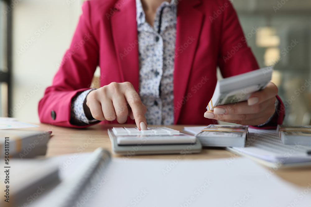Fototapeta premium Female accountant sits at her desk and counts money with calculator.