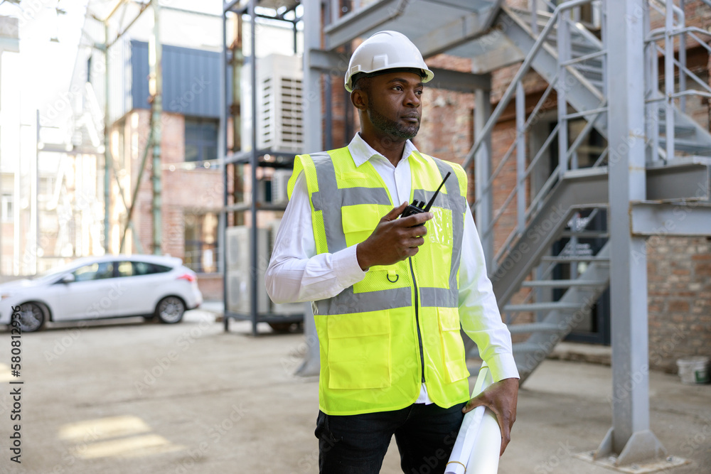 African american man controller in protective hardhat using walkie talkie for regulation work and building process. Concept of safety engineer work at construction site. African american man controller in protective hardhat using walkie talkie for regulation work and building process. Concept of safety engineer work at construction site.