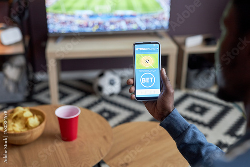Canvas Print Close up of male hand holding smartphone with online sports bets on screen while