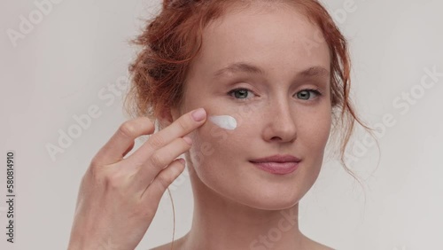 Slow motion portrait young woman uses creams of her face. Concept for fresh moisturized skin beautiful closeup cosmetic face happy healthy model. Young ginger hair woman take care of her skin.