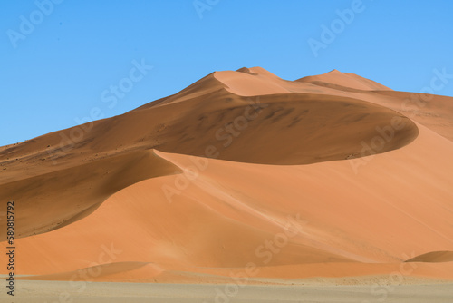 Rolling red desert dune in Deadvlei, white sand in foreground, blue cloudless sky