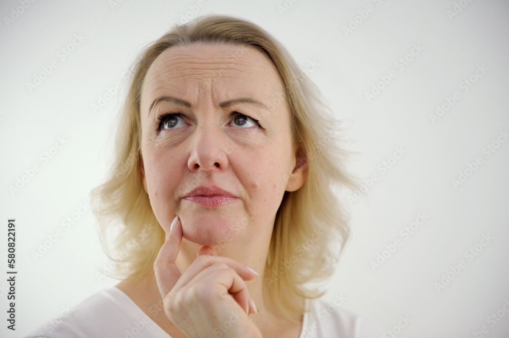 dissatisfied anxious Look at woman's hand near her chin think to worry woman raised her eyes up moved eyebrows one eyebrow higher than other wrinkled forehead white background unpleasant emotions dissatisfied anxious Look at woman's hand near her chin think to worry woman raised her eyes up moved eyebrows one eyebrow higher than other wrinkled forehead white background unpleasant emotions