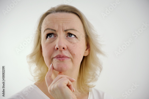 dissatisfied anxious Look at woman's hand near her chin think to worry woman raised her eyes up moved eyebrows one eyebrow higher than other wrinkled forehead white background unpleasant emotions