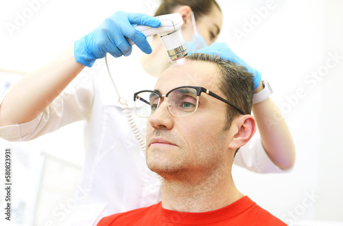 A cosmetologist-trichologist diagnoses the condition of a male patient's hair with gray hair using a trichoscope. photo