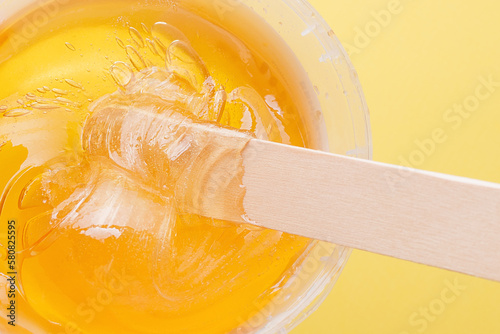 Liquid yellow sugar paste, wooden spatula on yellow background. Removing unwanted hair. Sugaring. Depilation. Epilation. Beauty. Top view.
