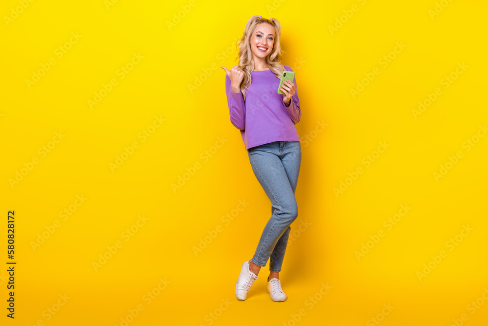 Full length photo of pretty funny lady dressed purple shirt writing modern device thumb emtpy space isolated yellow color background Full length photo of pretty funny lady dressed purple shirt writing modern device thumb emtpy space isolated yellow color background