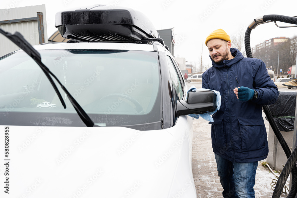 Man wipes american SUV car mirror with a microfiber cloth after washing in cold weather.