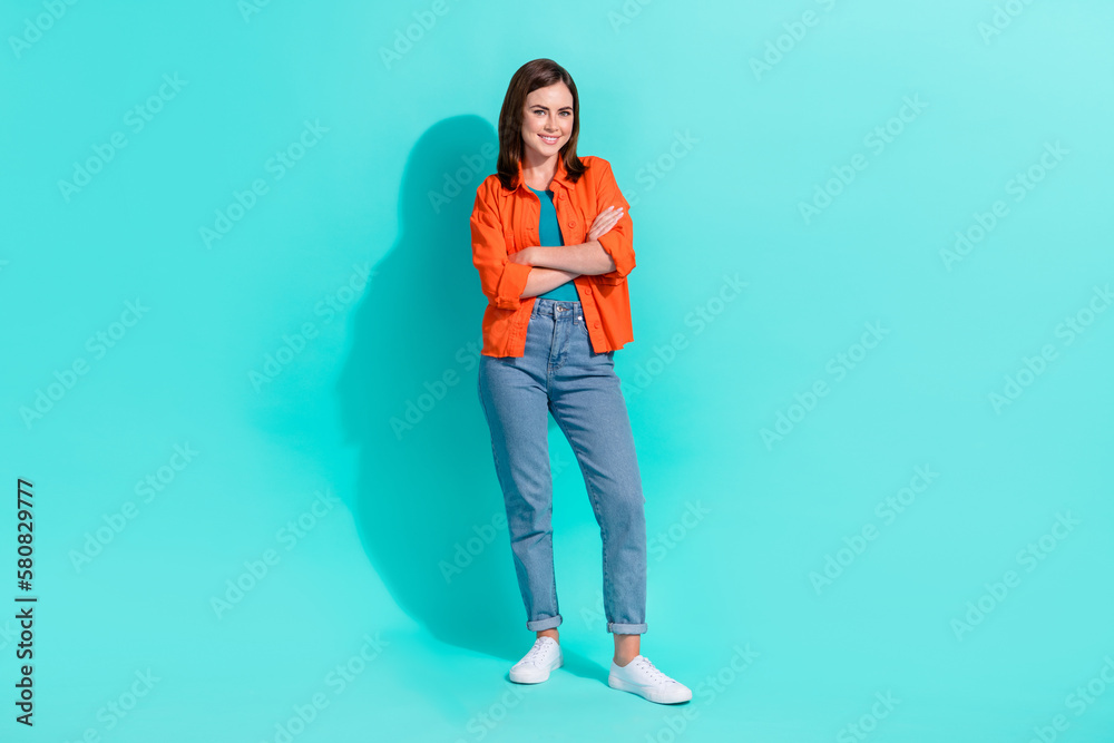 Full length photo of pretty confident lady wear orange shirt smiling arms folded isolated teal color background Full length photo of pretty confident lady wear orange shirt smiling arms folded isolated teal color background