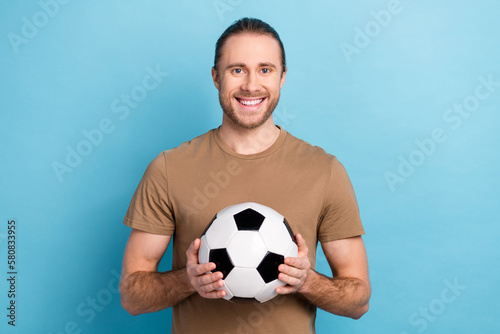 Photo of cheerful good mood man wear beige t-shirt holding football ball isolated blue color background