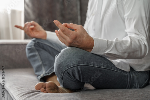 Close-up of a man sitting on a sofa in the lotus position. Close-up. Side view.