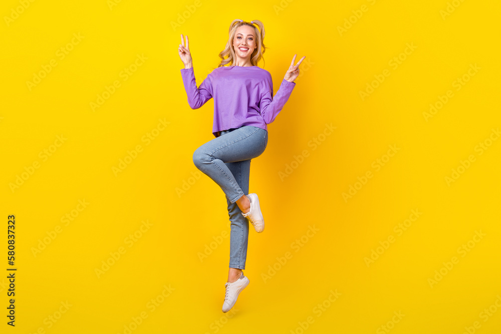 Full length photo of lovely young lady jumping flight showing v-sign hands wear trendy purple garment isolated on yellow color background