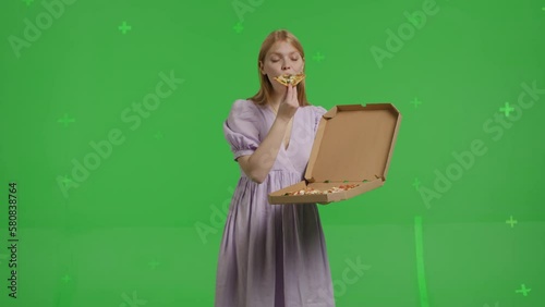 A young attractive red-haired woman holding a box of thin Italian pizza. Smiling girl in a linen dress eating fast food on a green background photo