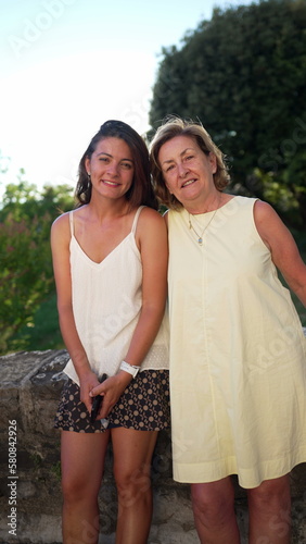 Portrait of mature woman and young daughter in law posing for camera standing outdoors during summer day. Two happy women of different generations in Vertical Video