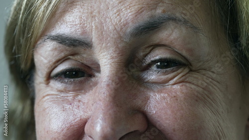 Portrait face close up of a senior woman opening eyes at camera with happy expression. Macro eyes of a mature female person in 70s