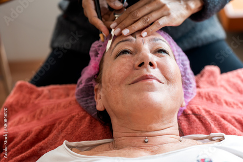 Crop anonymous female cosmetologist measuring proportions of eyebrows during microblading procedure in beauty salon