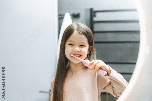 Happy little girl brushing her teeth in front of a bathroom mirror. Morning hygiene.